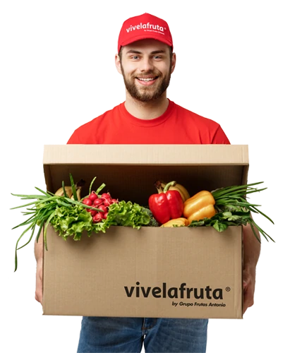 Imagen de un hombre sonriente con barba, vestido con vaqueros, camiseta roja y gorra roja con el logo de Vivelafruta. Sostiene una caja de frutas y verduras frescas de la marca.