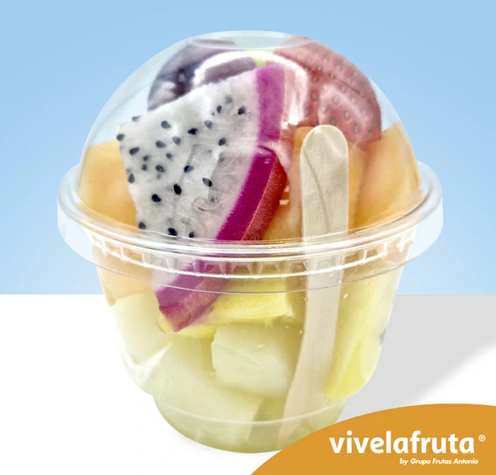 Un vasito de plástico transparente con 220 gramos de fruta fresca exótica, sobre un fondo azul. Se aprecian trozos de fresa, pitahaya, piña y melón.